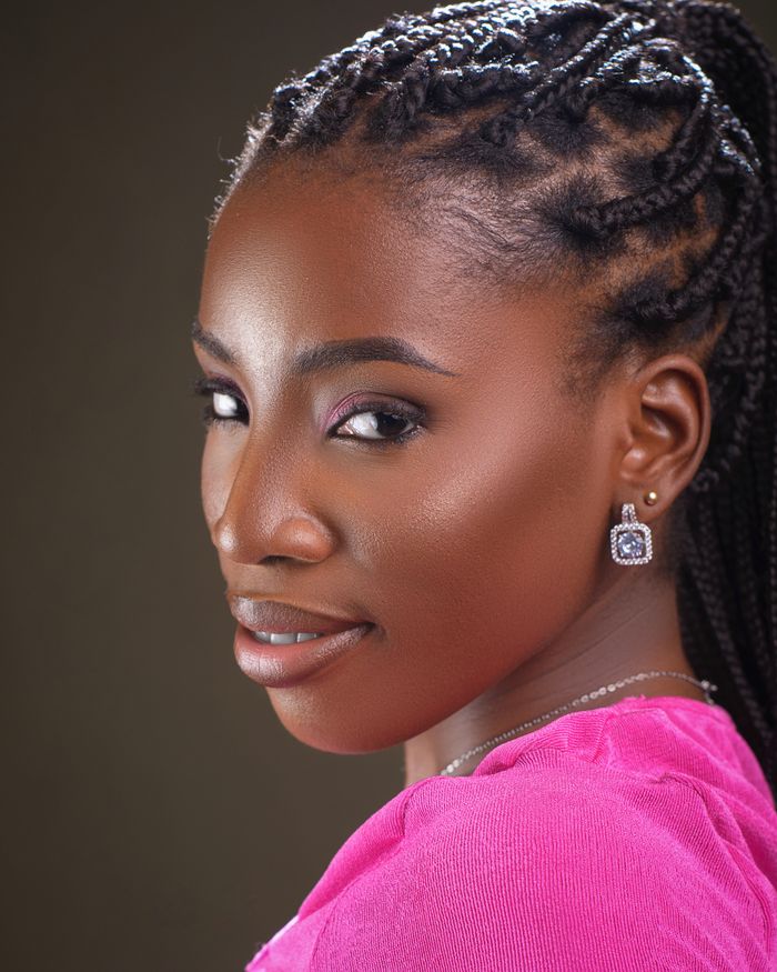 Close-up portrait of a smiling woman with intricate braided hair wearing earrings.
