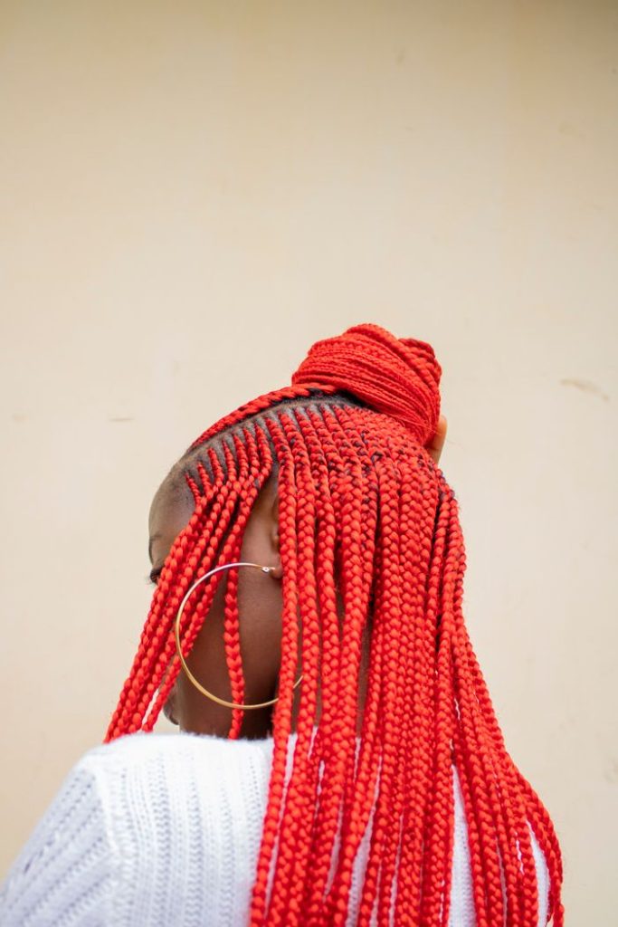 Close-up of a woman with vibrant red braided hair styled in a bun and large hoop earrings.